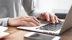 Close-up of man's hands scrolling and typing on a laptop.