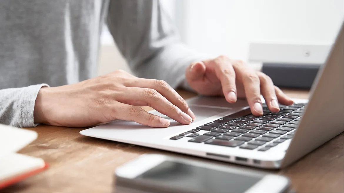 Close-up of man's hands scrolling and typing on a laptop.