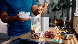 Close up of man adding Greek yogurt while preparing healthy smoothie in the kitchen.