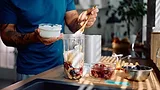 Close up of man adding Greek yogurt while preparing healthy smoothie in the kitchen.