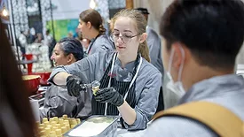 Young woman serving ice cream on a cone surrounded by other workers.