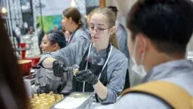 Young woman serving ice cream on a cone surrounded by other workers.