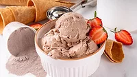 High protein chocolate ice cream A bowl if ice cream with strawberry slices, ice cream cones in the background and a spilled over container of protein powder.
