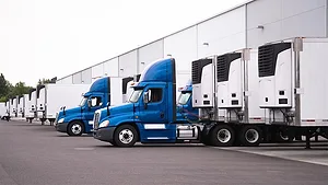 Blue semi-trucks and semi-trailers stand in row hardly near the warehouse Blue semi trucks and semi trailers stand in row hardly near the warehouse gate under loading and unloading process.