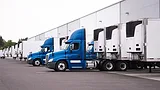 Blue semi-trucks and semi-trailers stand in row hardly near the warehouse Blue semi trucks and semi trailers stand in row hardly near the warehouse gate under loading and unloading process.