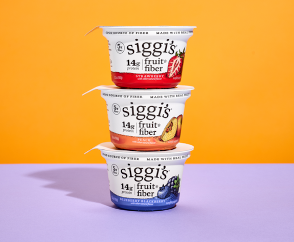 A tower of three different flavors of Siggi's 14g Fruit Fiber on a lavender-colored table and an yellow-orange background.