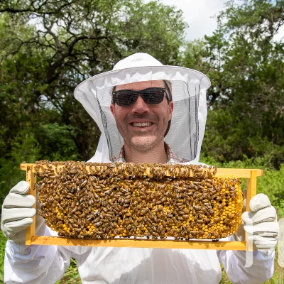 Keith Seiz in a protective suit holding up a honeycomb.
